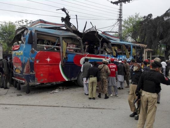 Policemen and rescue officials walk near a bus damaged in a bomb blast in Peshawar